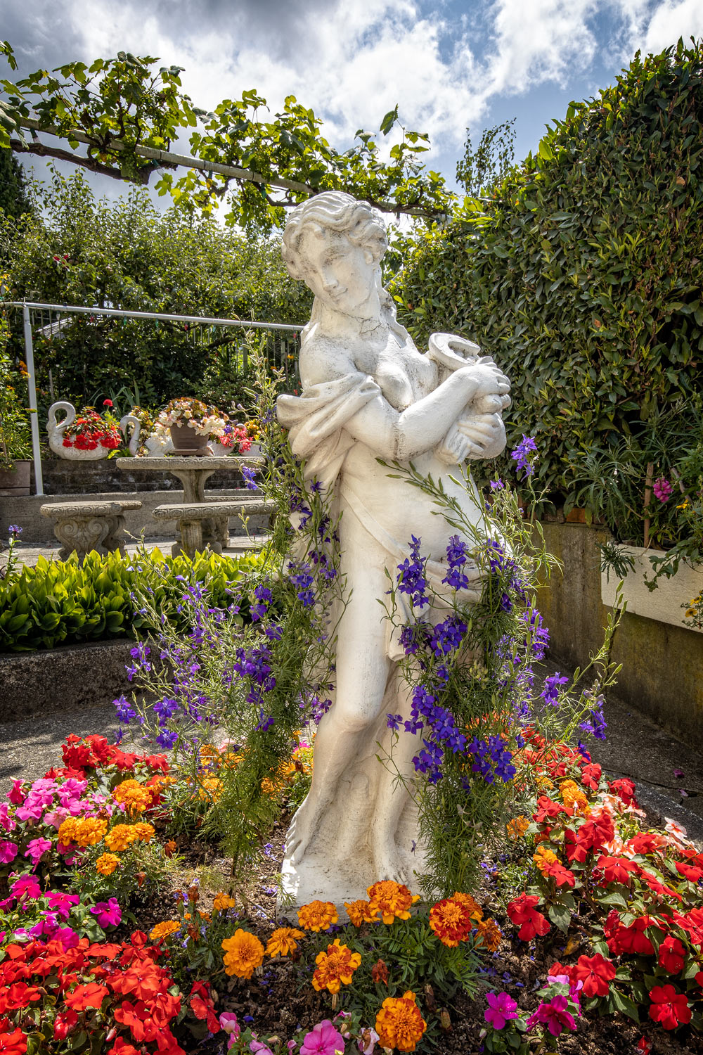 Statue of a Lady standing in a garden surrounded by flowers.